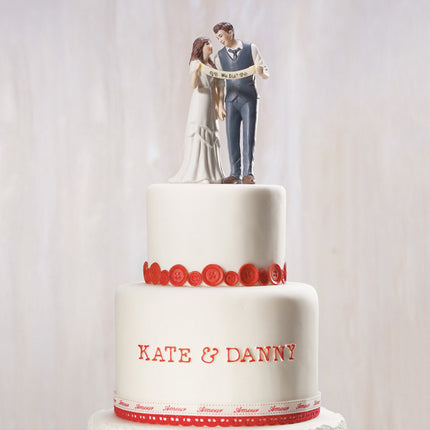 An Indie Wedding Couple Porcelain Cake Top on top of a red and white wedding cake.